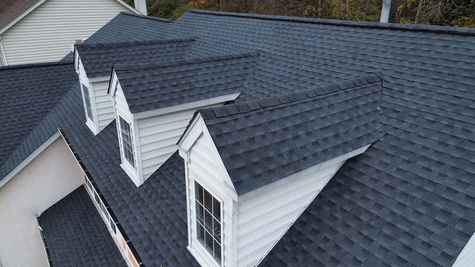 Close aerial view of a finished charcoal architectural shingle roof with three white dormers and a valley running between them