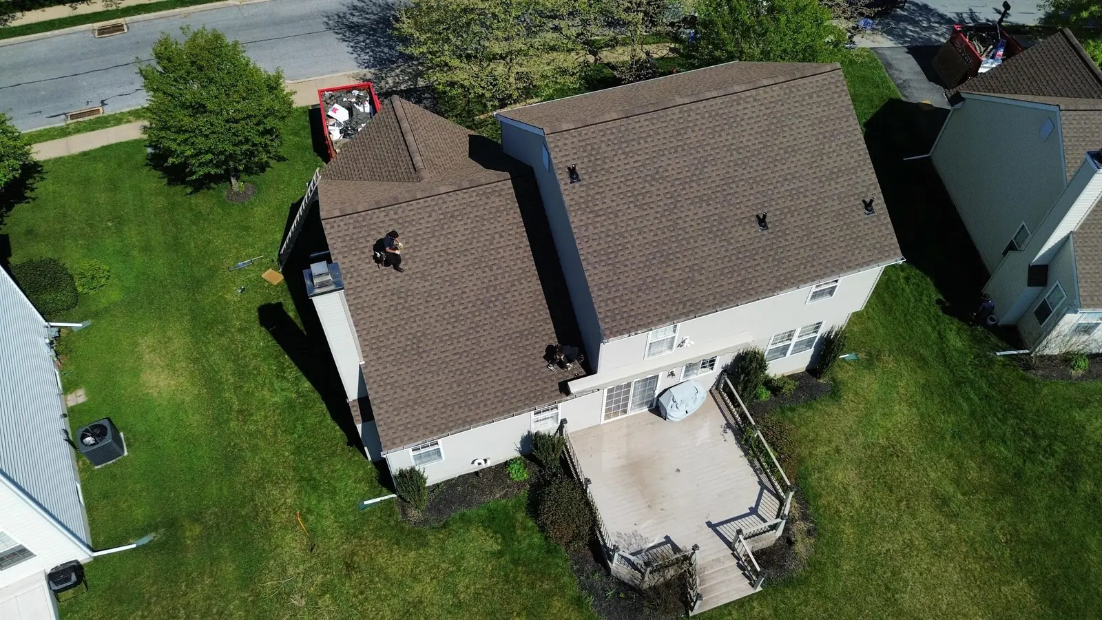 Two of our crew standing on the slopes of a brown shingle roof with the tear off trailer parked at the curb below