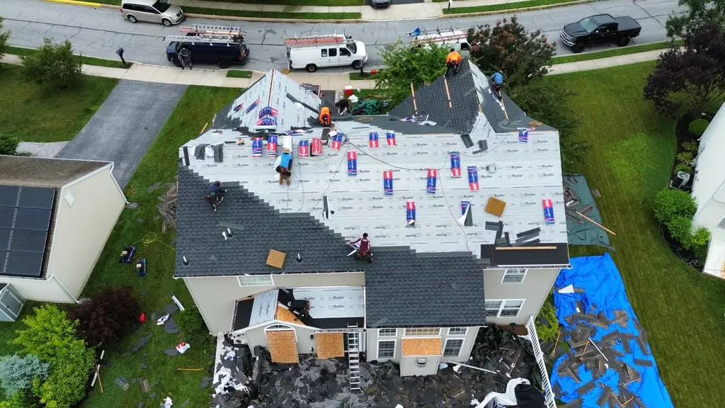 Aerial view of our crew replacing a roof, with a blue tarp spread over the landscaping and work vans parked along the street