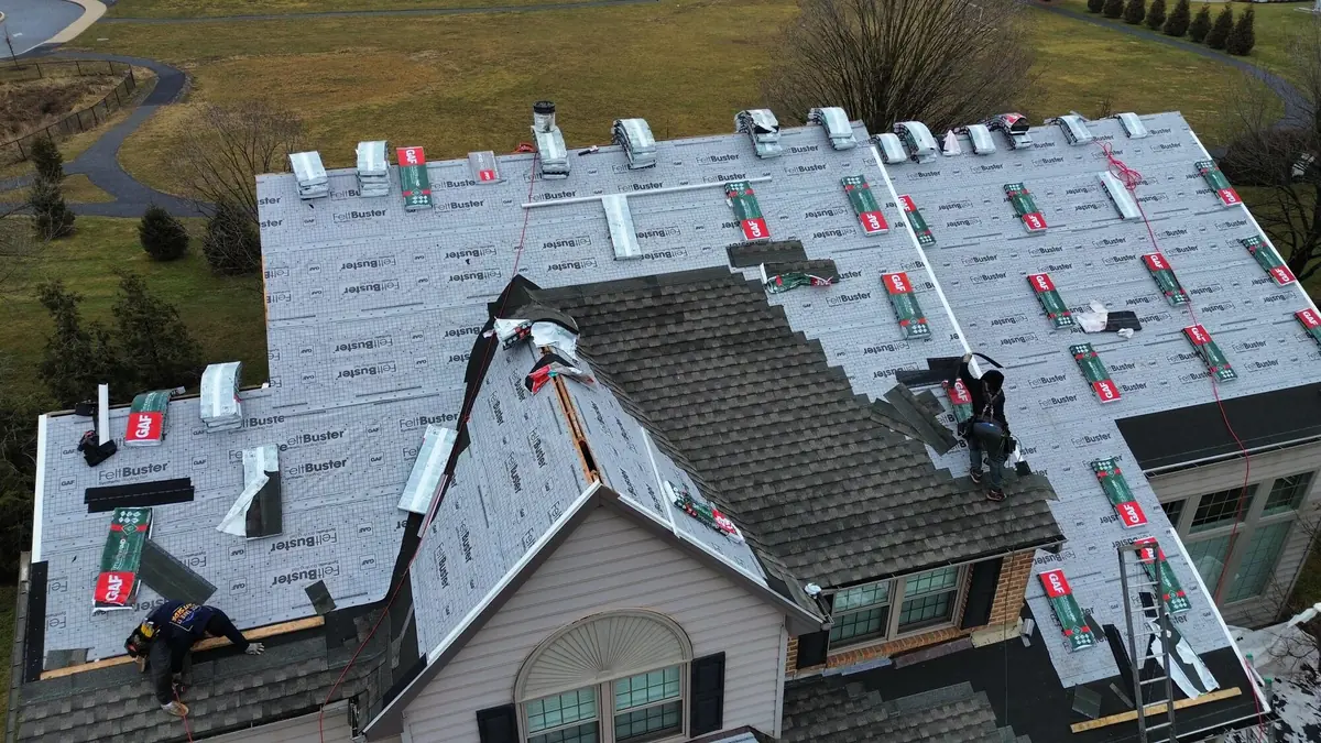 Aerial view of a wide roof covered in GAF FeltBuster synthetic underlayment with GAF Timberline bundles staged and two roofers working the ridge
