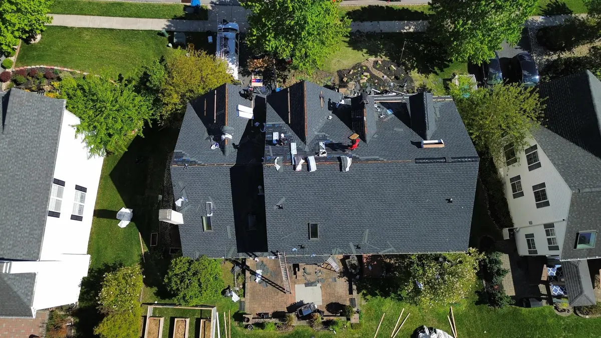 Aerial view of a large home with a completed dark charcoal shingle roof and a few bundles left along the ridge