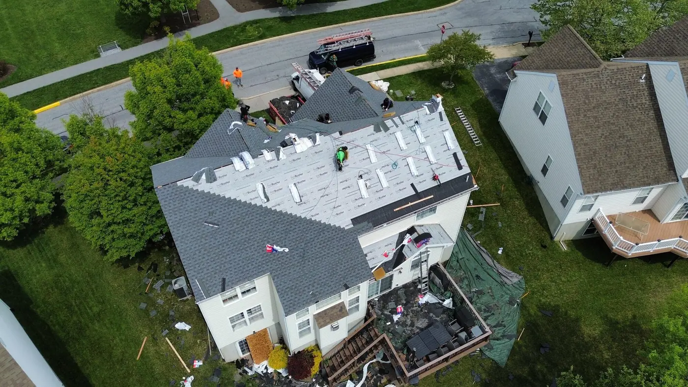 Aerial view of a roof replacement in progress with new dark shingles on the front slopes, underlayment on the back and a roofer working in the middle