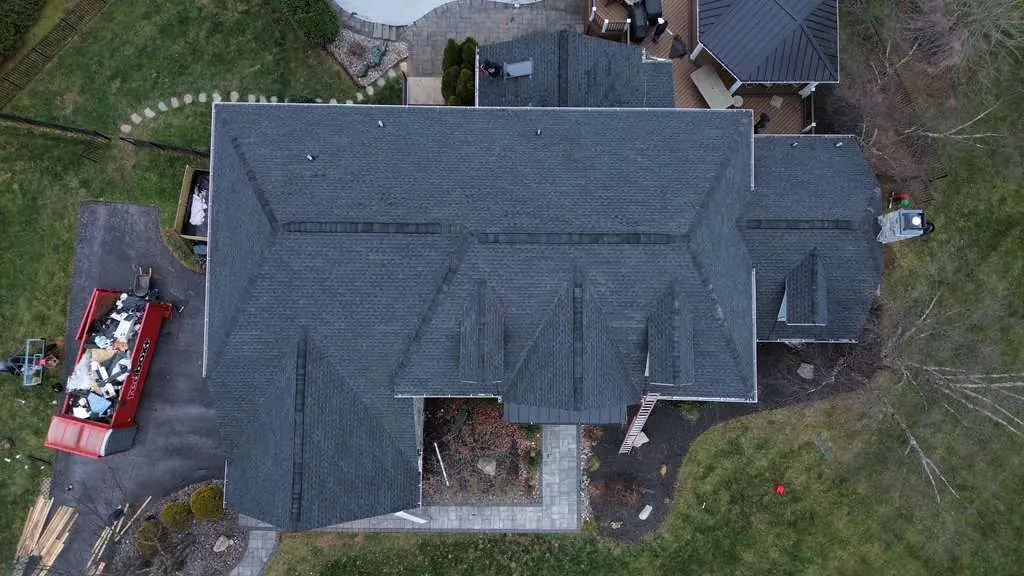 Top down aerial of a finished slate gray shingle roof with the tear off debris already loaded into a red dump trailer in the driveway