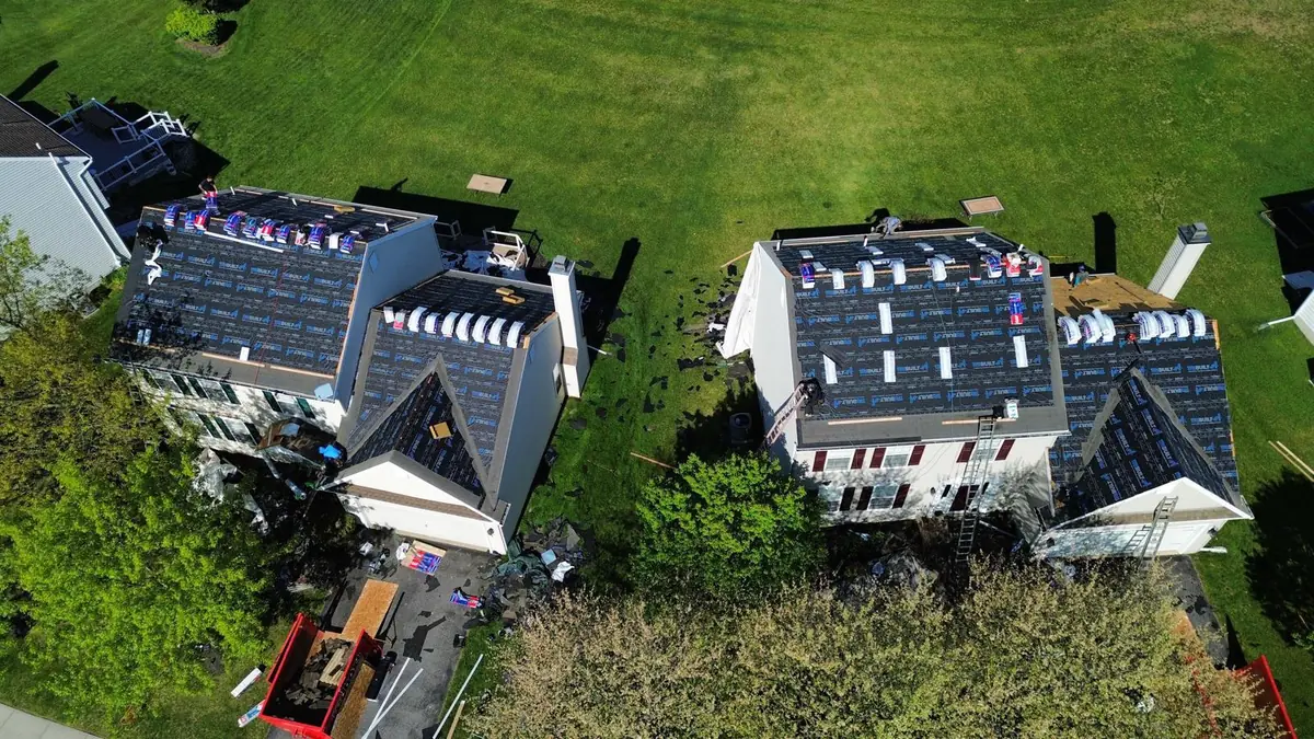 Aerial view of two adjacent homes both stripped to underlayment with shingle bundles staged across all of the slopes