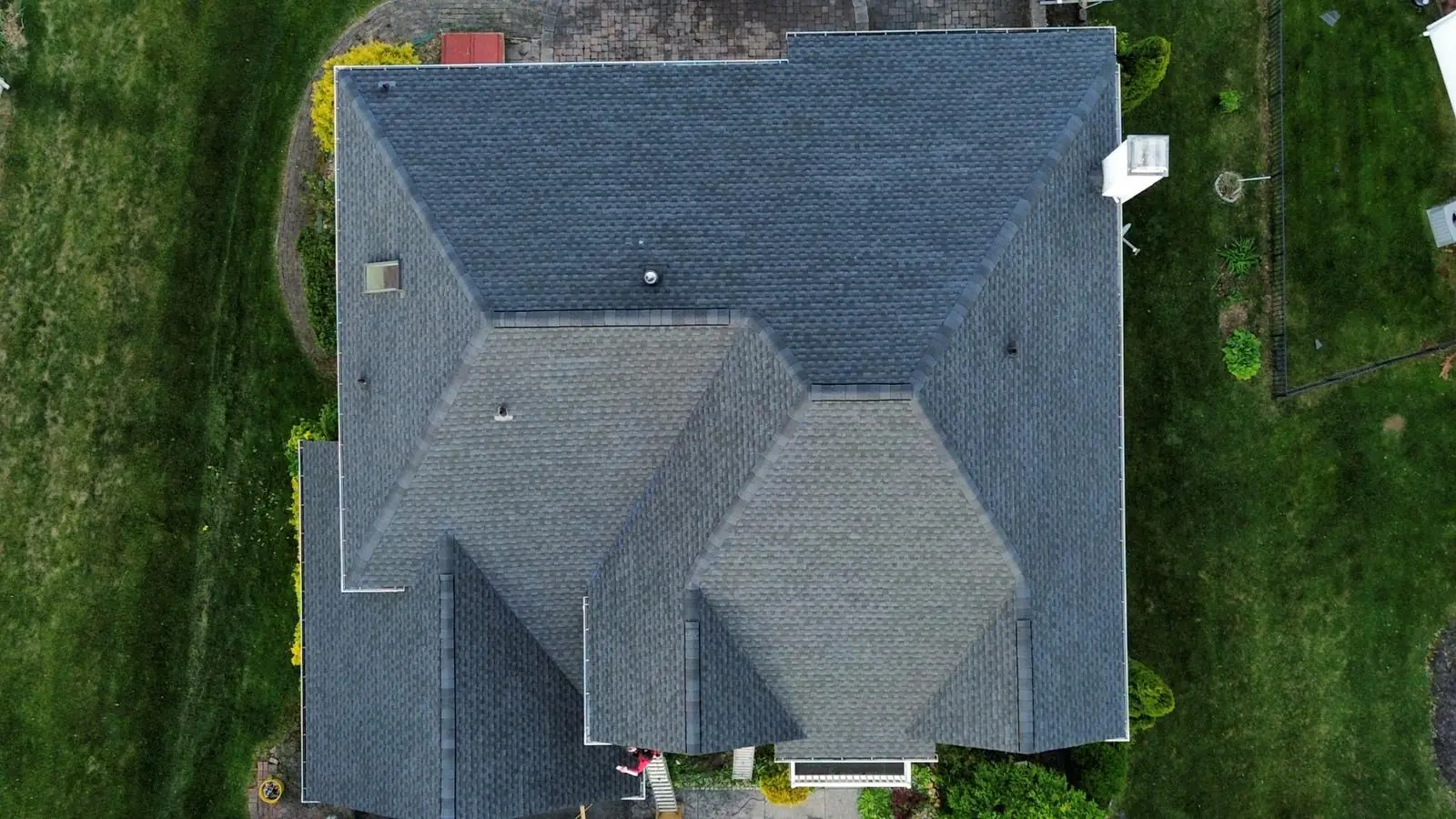 Straight down aerial of a large hip roof finished in weathered wood colored architectural shingles surrounded by lawn