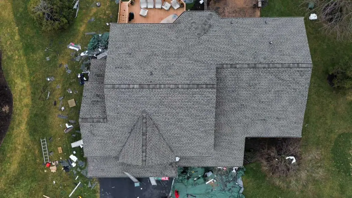 Top down aerial of a weathered gray shingle roof with faded, worn shingles and debris and tarps in the yard below